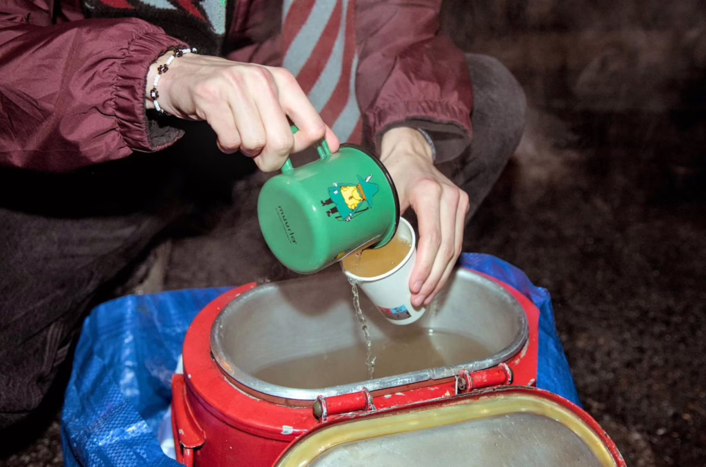 A closeup of a person's hands distributing tea into a paper cup